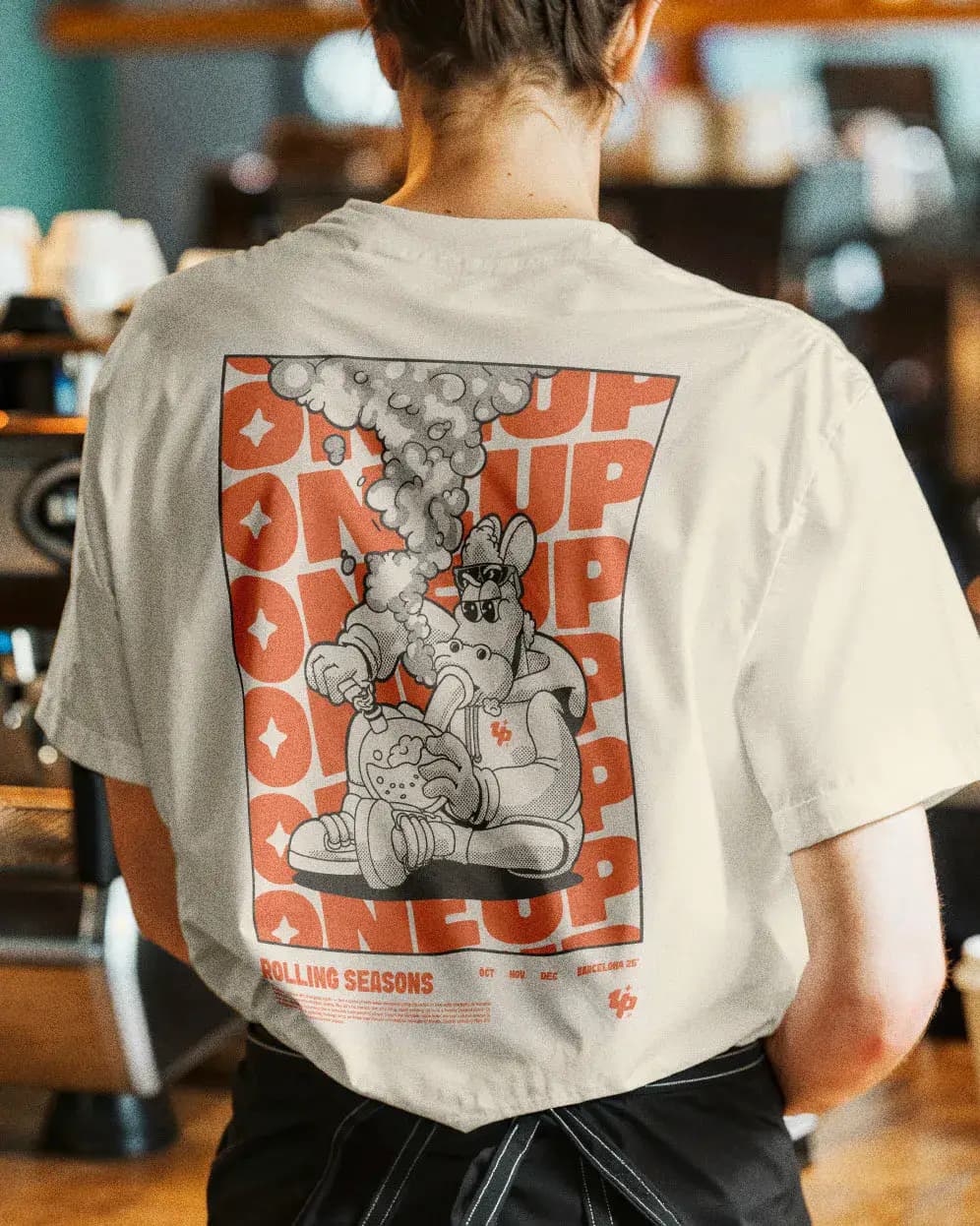 Back view of person wearing white ONEUP graphic t-shirt featuring signature mascot artwork and orange print design.