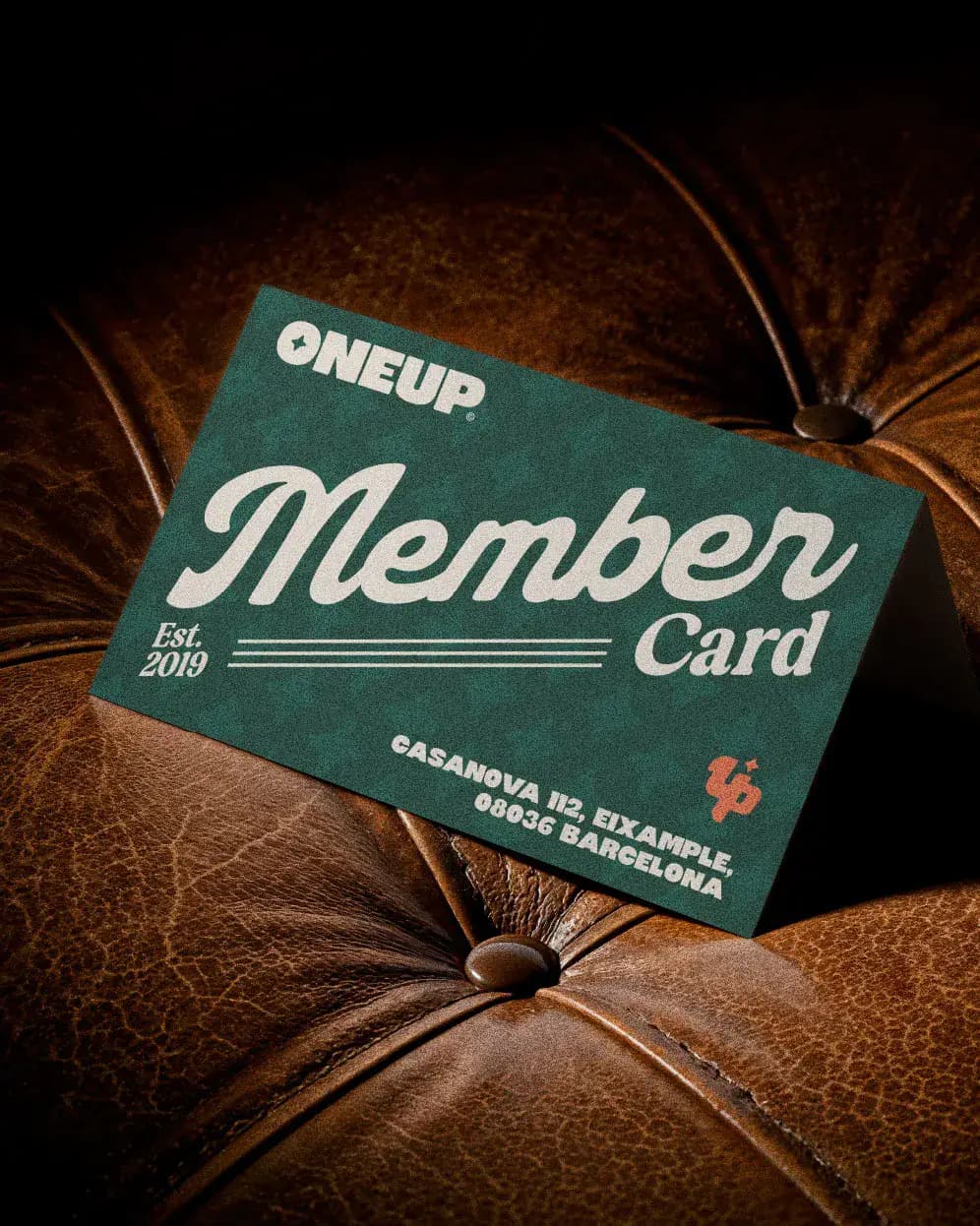 ONEUP member card placed on leather chair showing club branding and Eixample Barcelona address.